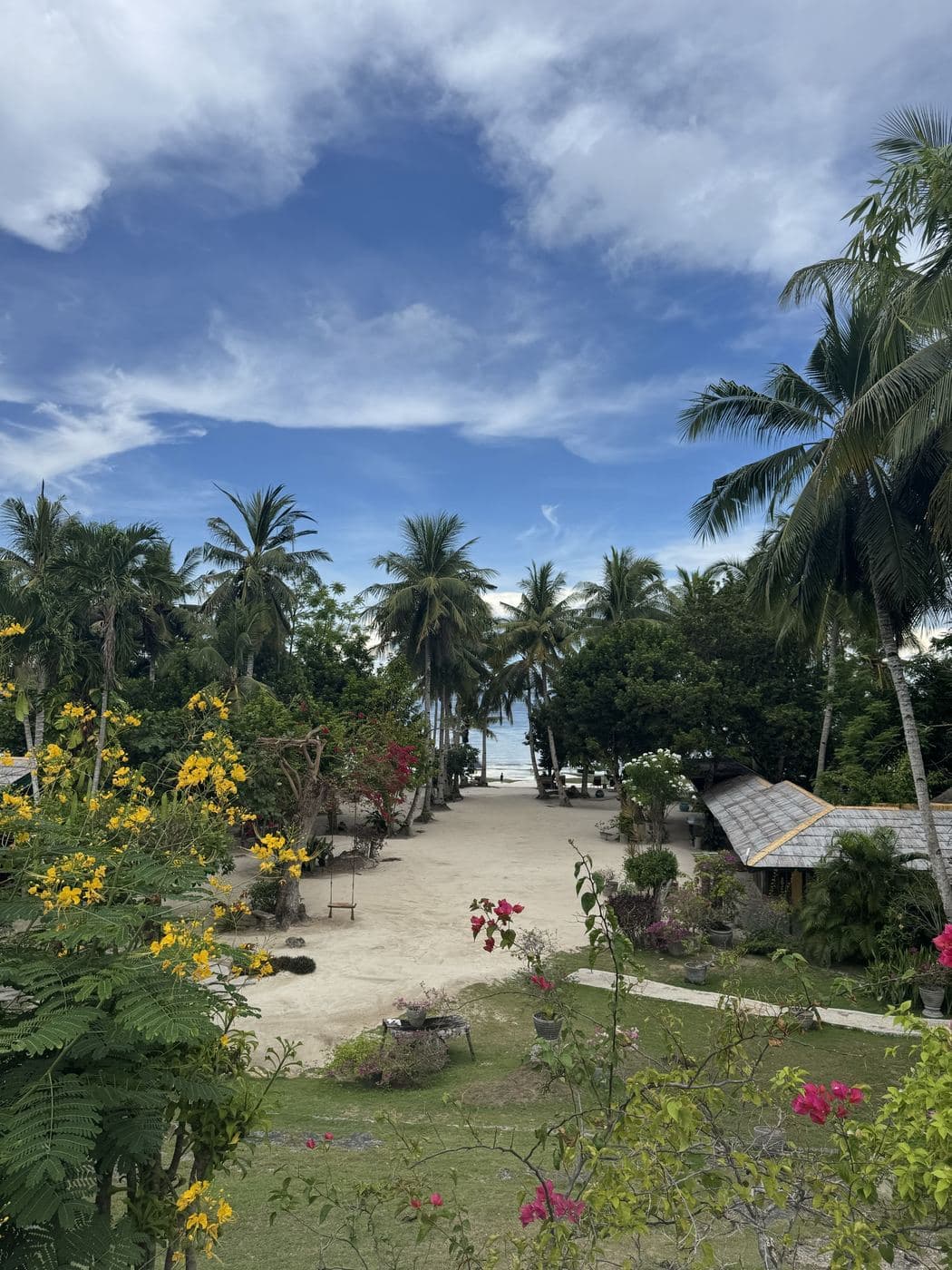 A sandy path through a tropical garden with palms and flowers leading to the beach