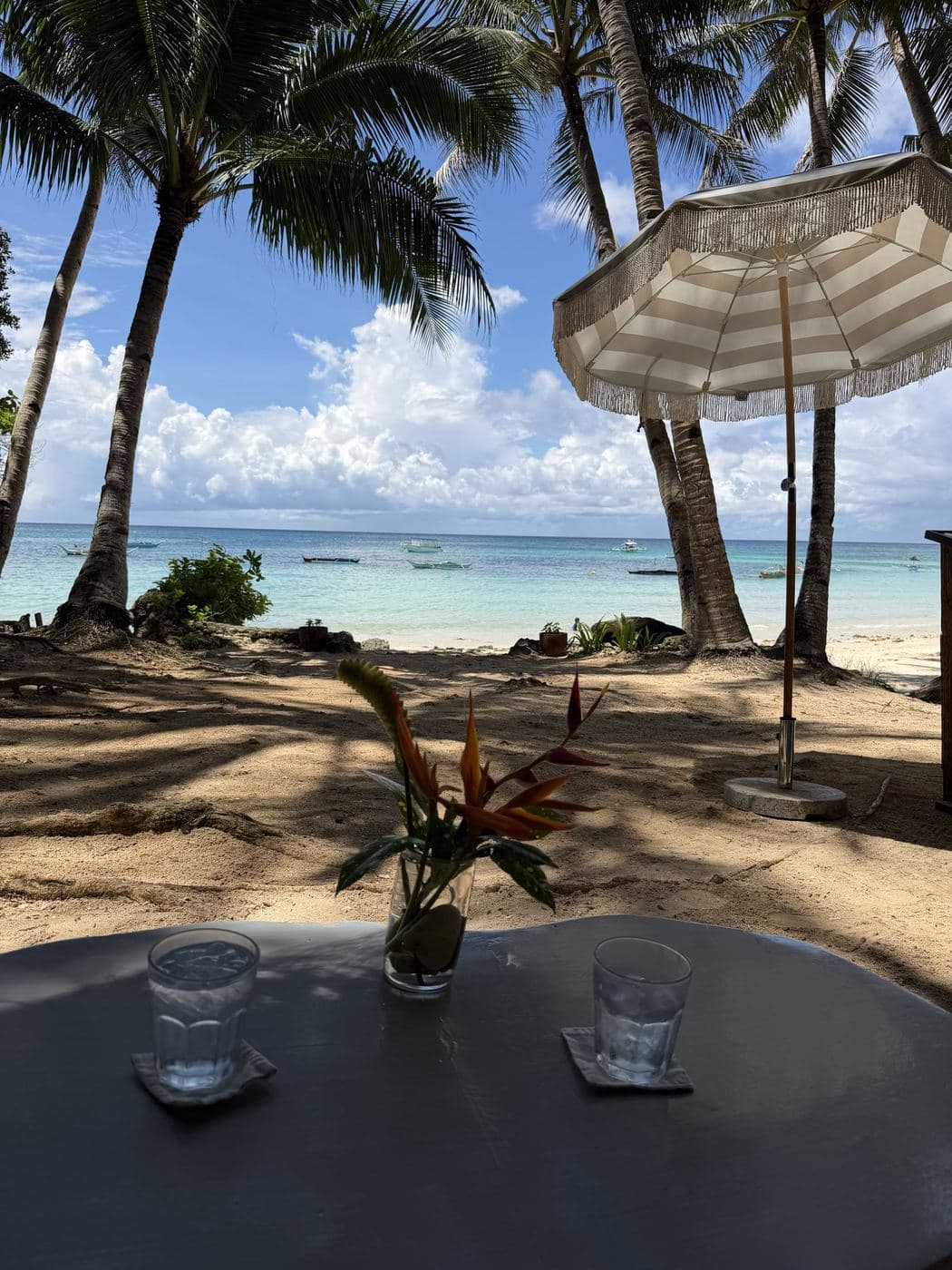 Palm trees and a beach umbrella over a turquoise Boracay bay