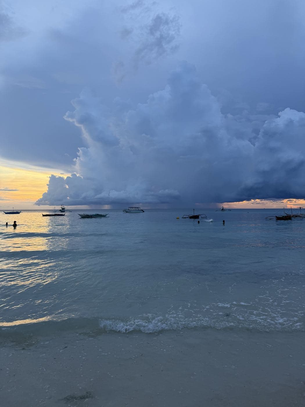 Sunset over calm water with boats and towering clouds in Boracay